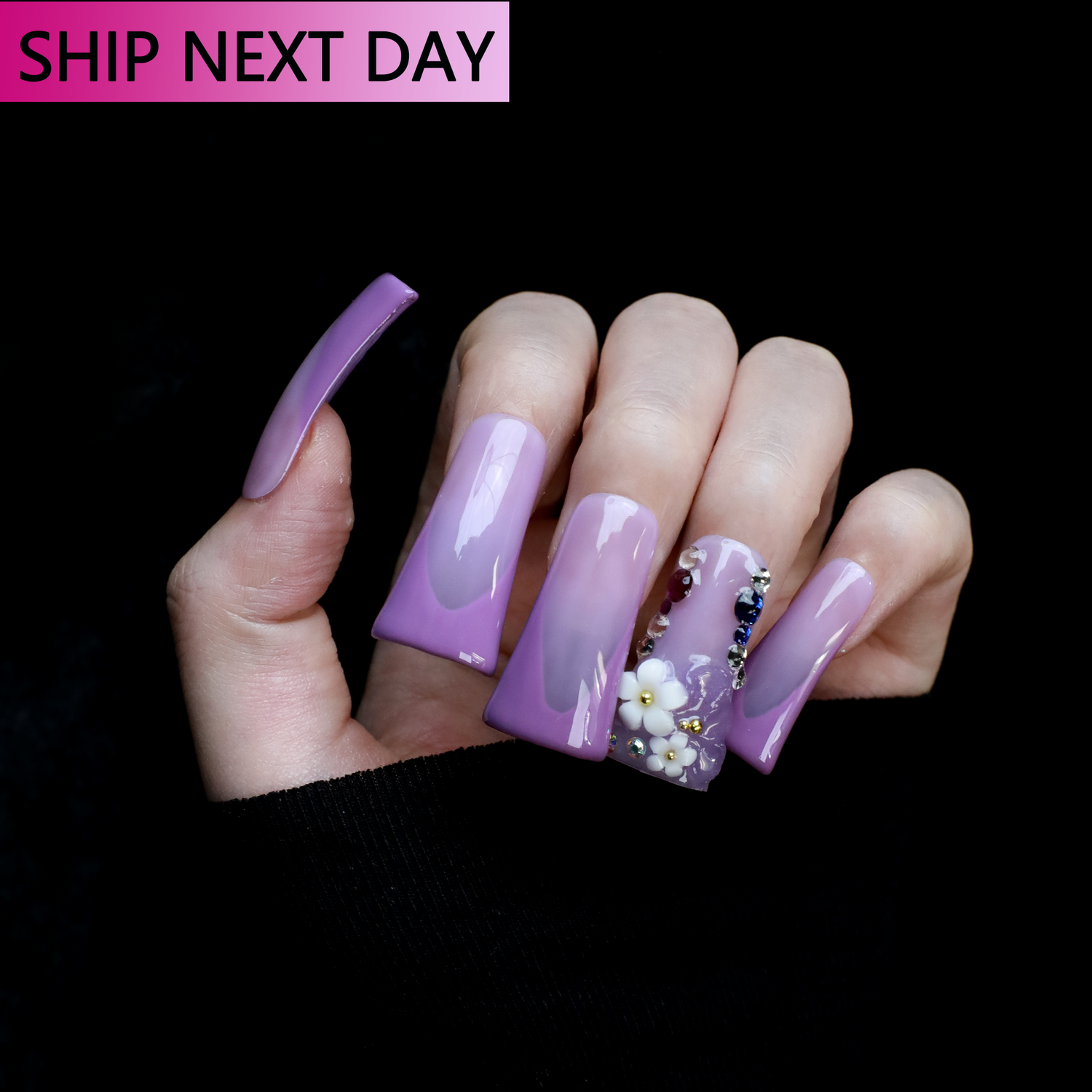 A hand displays We Do Nails Purple Floral Long Duck Press-On Nails with ABS material for durability, featuring intricate French nail art with white flowers and decorative gems. A SHIP NEXT DAY label appears on the sleek black background.