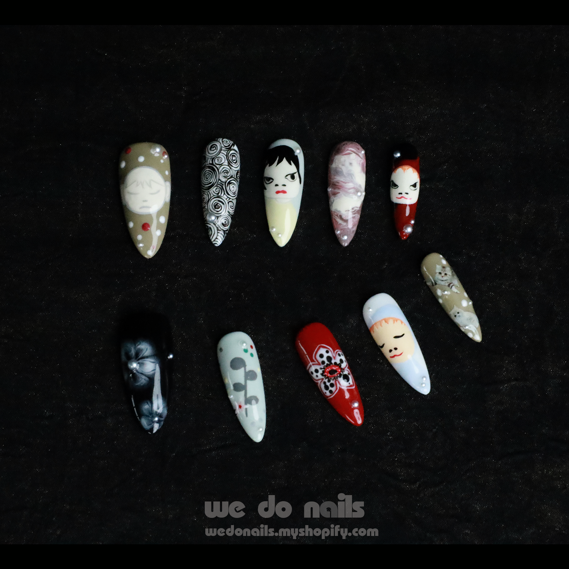 A hand with We Do Nails Cartoon Cuties Press-On Nails, featuring faces, abstract designs, and geometric shapes on a black background, holds a white teacup.