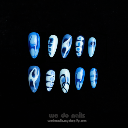 A person with Azure Waves Press-On Nails by We Do Nails, showcasing oceanic beauty and geometric designs, holds a small white handbag. The black background highlights the nails and bag, accentuating the nail arts blue waves.