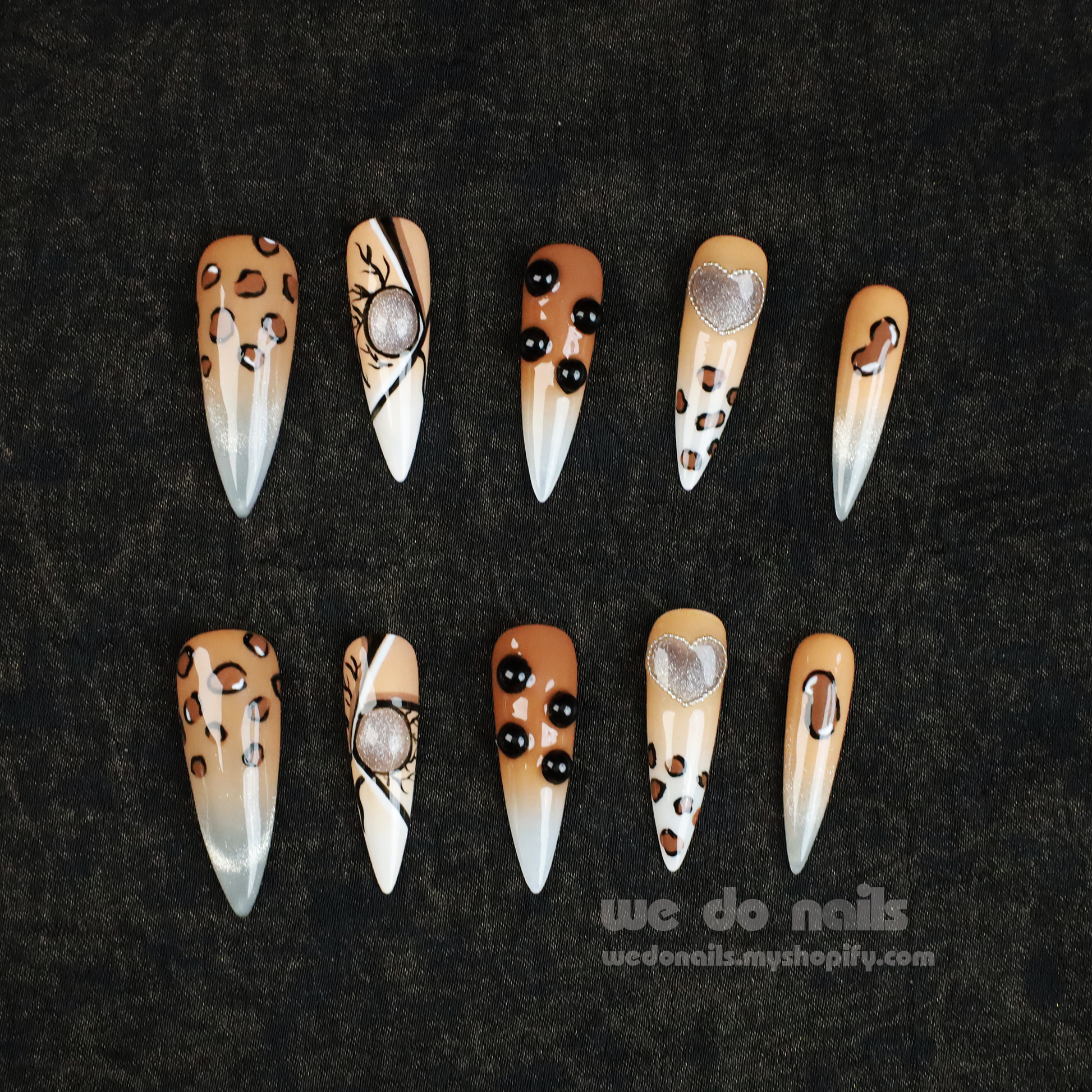 A hand with long, artistic nails featuring chic black and gold designs holds a white mug. The 3D Fierce Leopard Brown Press-On Nails by We Do Nails boast geometric shapes and rhinestones, embodying true Leopard Power.