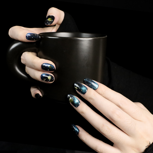 Hands holding a matte black mug. The nails, adorned with We Do Nails Nautical Navy Blue Stripes Press-On Nails, feature a cosmic theme of stars and planets, with one nail showing a striking 3D yellow flower accent.