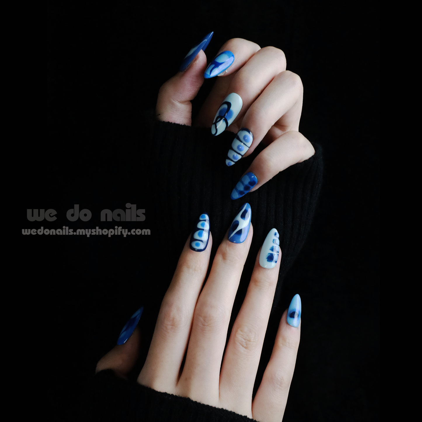 A person with Azure Waves Press-On Nails by We Do Nails, showcasing oceanic beauty and geometric designs, holds a small white handbag. The black background highlights the nails and bag, accentuating the nail arts blue waves.