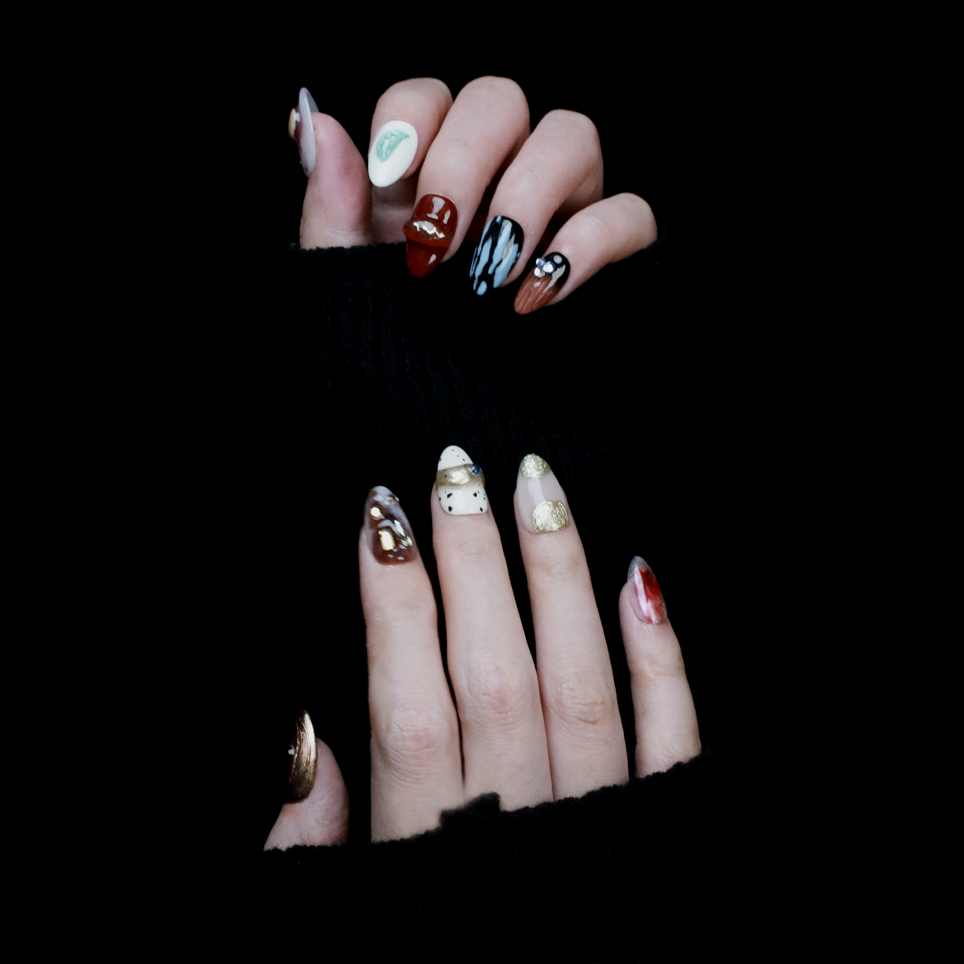 A hand elegantly displays Avant-Garde Luxe Press-On Nails by We Do Nails against a black backdrop. These nails, featuring 3D embellishments, boast white, maroon, and black hues with intricate patterns and metallic accents.