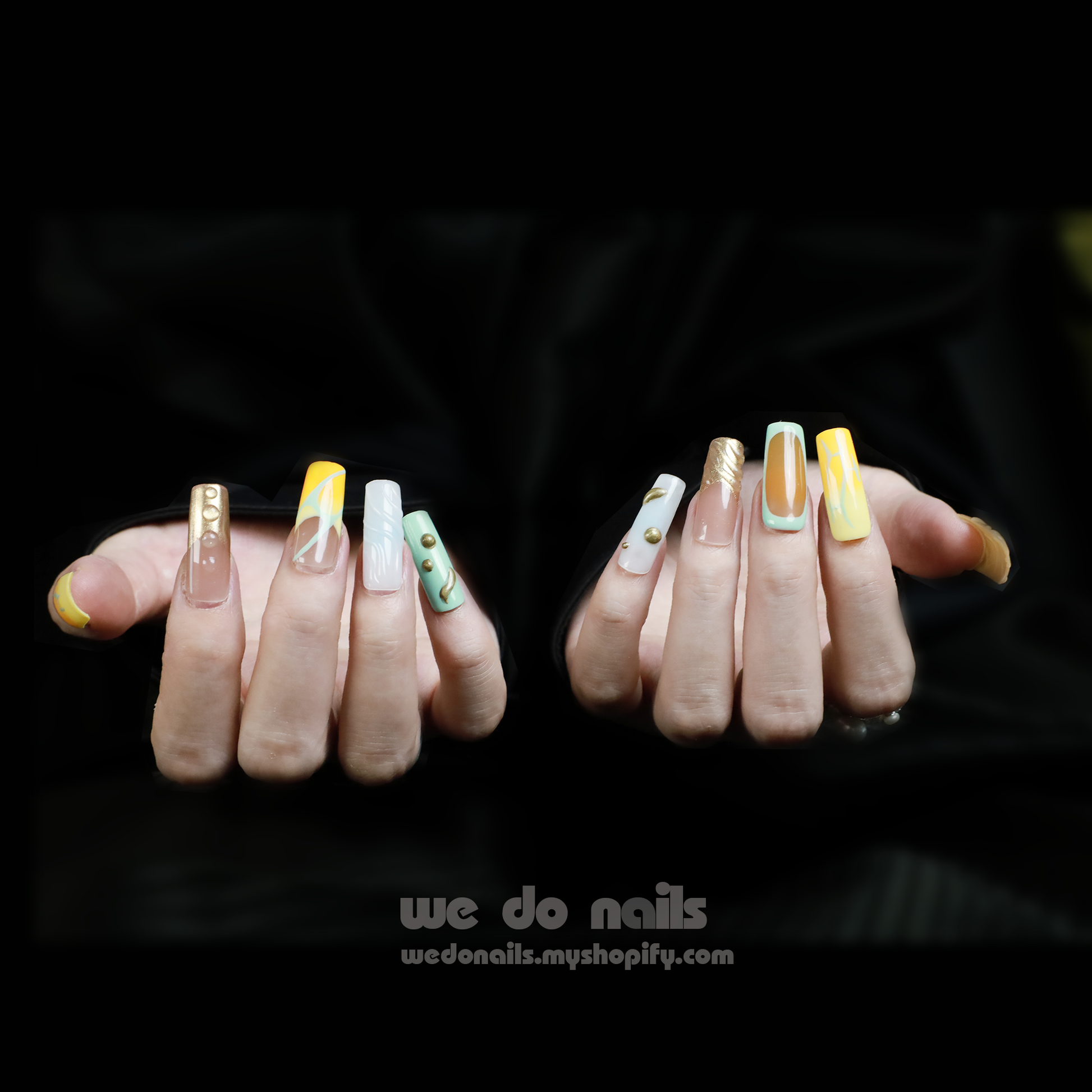 Close-up of manicured hands featuring Earths In Motion Press-On Nails by We Do Nails, showcasing intricate 3D designs with gold, white, and green patterns and marbling on a black background.